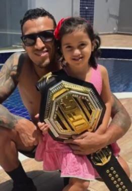 Talita Roberta Pereira husband Charles Oliveira and daughter Tayla posing with the UFC championship belt.